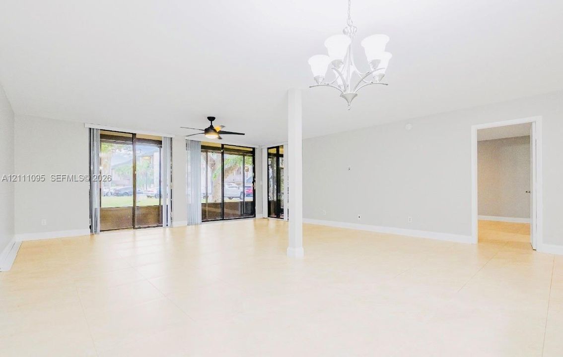 Large format tile flooring, multi-panel sliding glass doors, overhead ceiling fan with light fixture, and decorative multi-arm chandelier