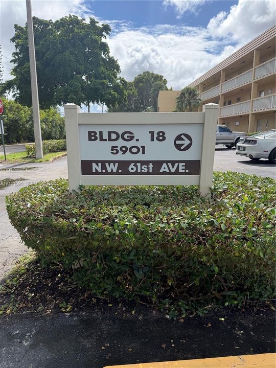 Directional property signage with building and street identification surrounded by manicured shrubbery