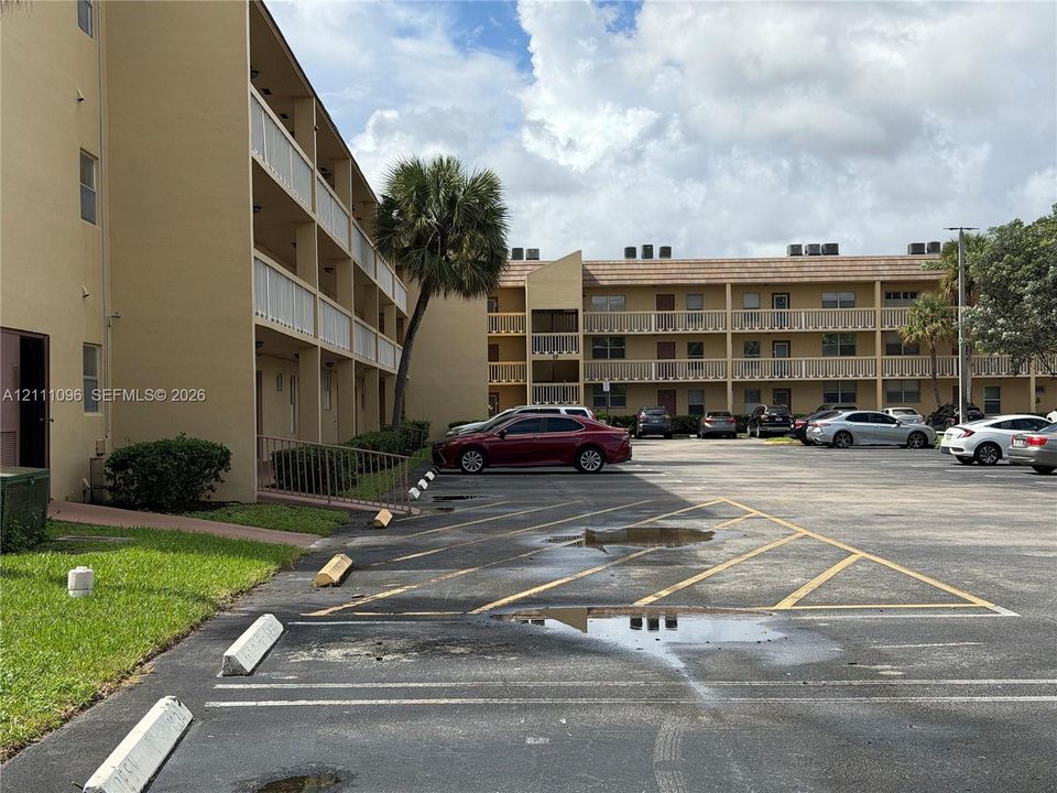Multi-story exterior featuring tan stucco siding, covered walkways with metal railings, and a surface parking lot