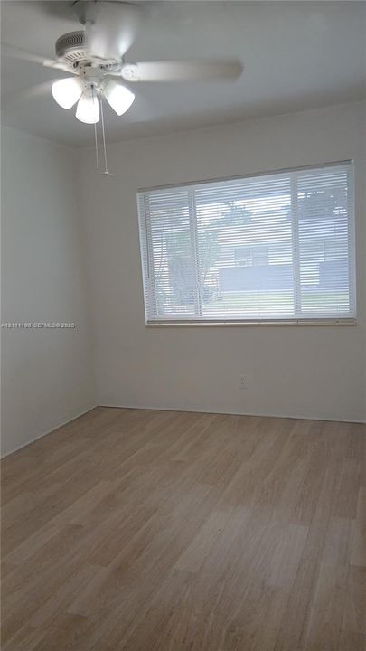Interior space featuring light-toned wood-finish flooring, a ceiling fan with integrated lighting, and a large multi-pane window