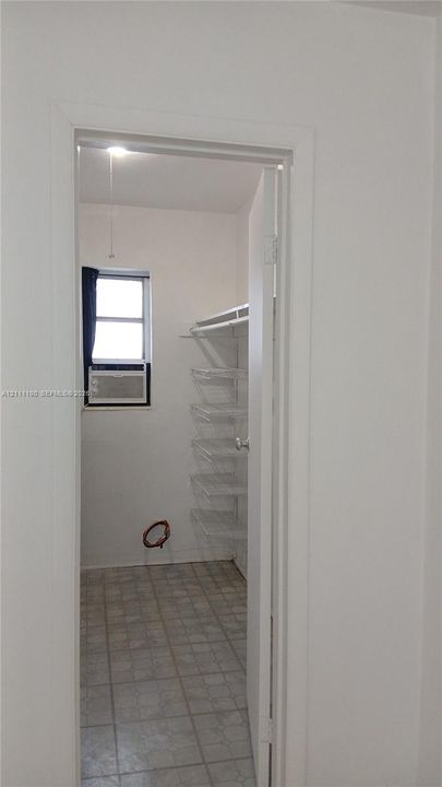 Storage room featuring tile flooring, a window, integrated wall shelving, and a hanging rod