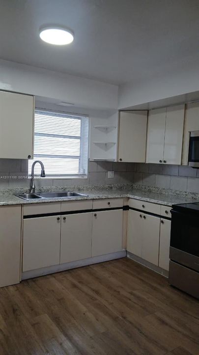 Kitchen featuring stone-finish countertops, wood-finish flooring, undermount dual-basin sink with arched faucet, and built-in cabinetry with open corner shelving