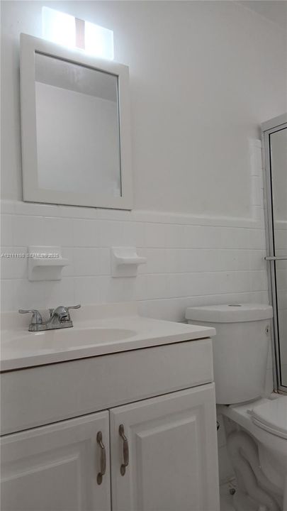 Bathroom vanity with a white cabinet, integrated sink, metal faucet, and wall-mounted mirror, featuring white subway tile wall surround