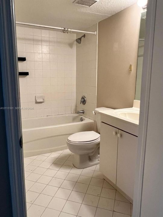 Bathroom featuring a white vanity cabinet with a molded sink, ceramic tile flooring, a shower-tub combination with white wall tile, and built-in shelving