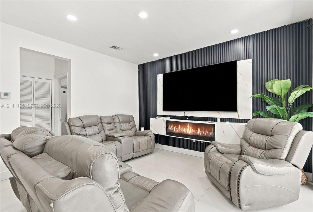 Living area featuring a floor-to-ceiling dark vertical slat accent wall, built-in media console with stone-patterned surfaces, integrated electric fireplace, and recessed ceiling lighting