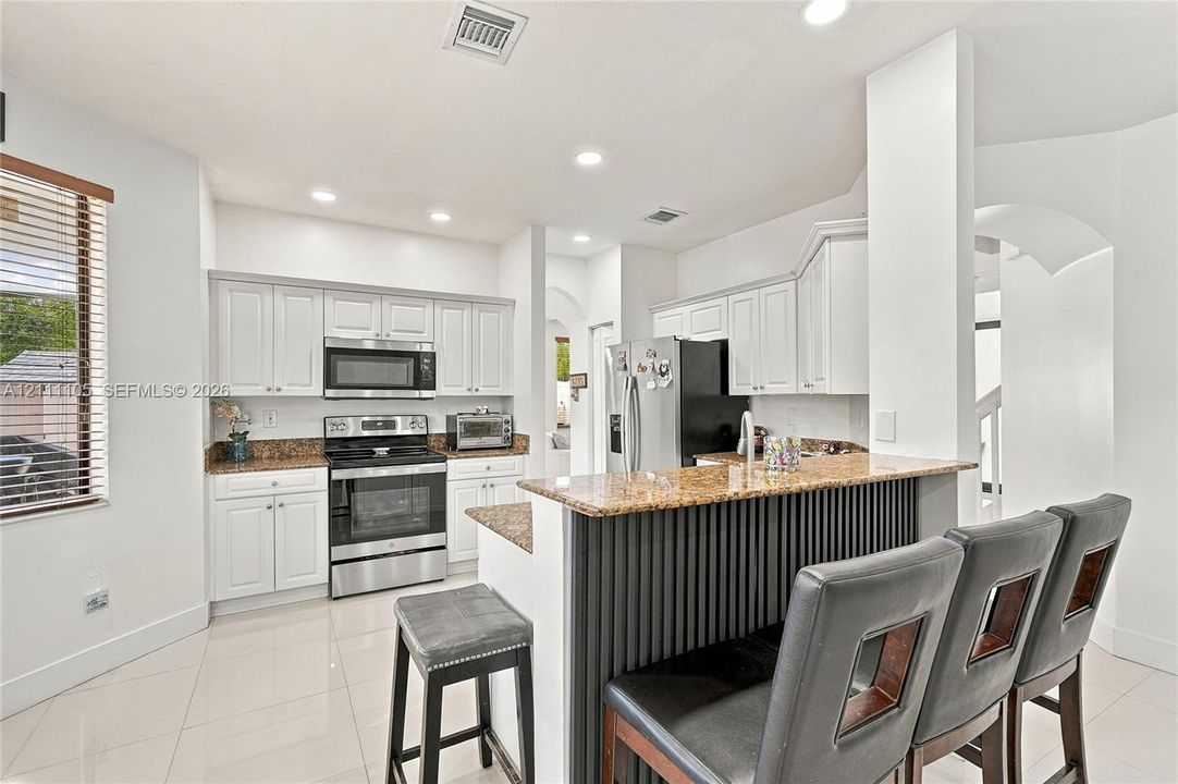 Kitchen featuring white cabinetry, stone-surface countertops, stainless steel appliances, recessed lighting, and a slatted breakfast bar