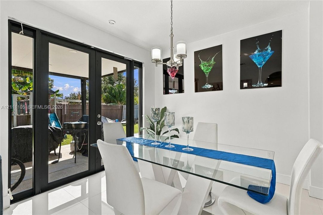 Dining space featuring polished tile flooring, black-framed French doors, and a brushed nickel multi-light chandelier
