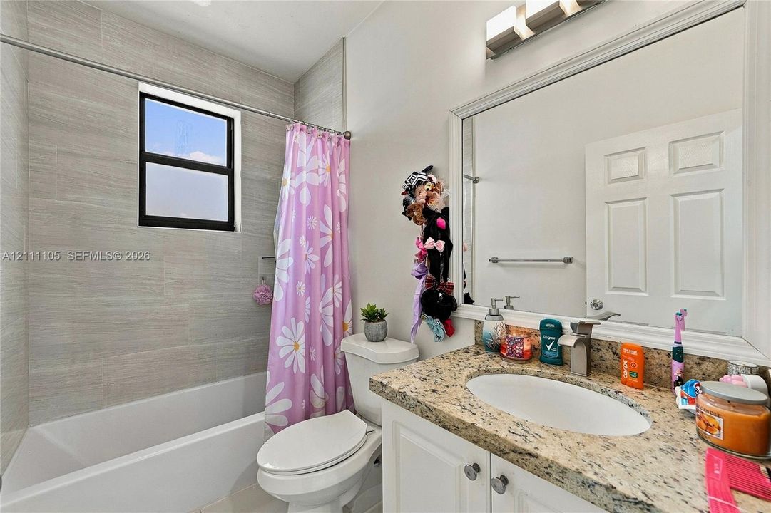 Full bathroom featuring a stone-patterned countertop vanity with an integrated sink, floor-to-ceiling neutral wall tile surrounding the bathtub, and a large wall-mounted mirror with an overhead light fixture