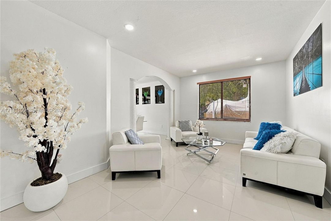 Living space featuring light-toned tile flooring, recessed lighting, and a prominent arched entryway