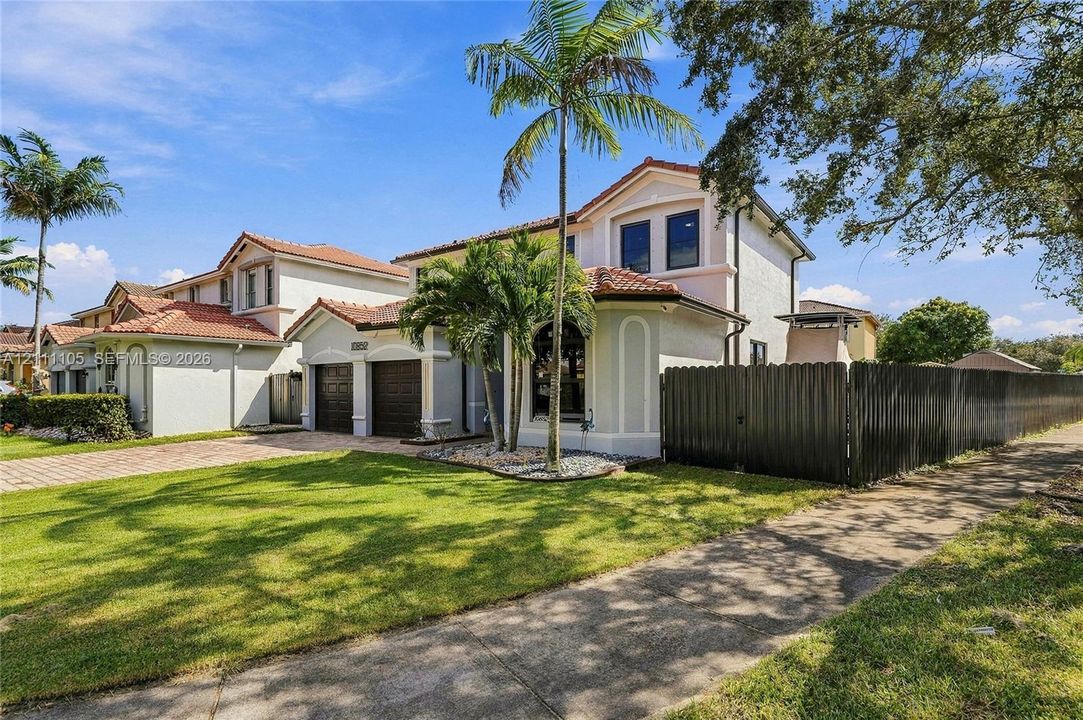Two-story stucco exterior featuring a terracotta tile roof, two-car garage, arched window accents, and a privacy fence