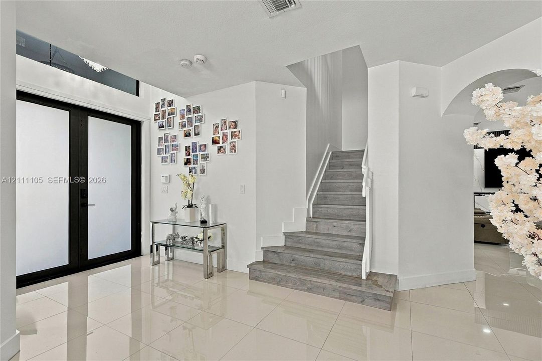 Foyer featuring double entry doors with frosted glass, high ceilings, large-format polished tile flooring, and a staircase with wood-finish treads and a white metal railing