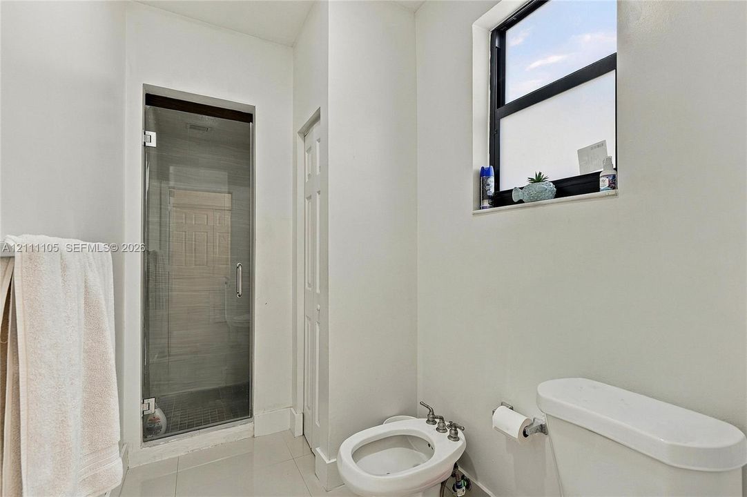 Walk-in shower with a glass door, floor-to-ceiling tile, and window with a dark frame