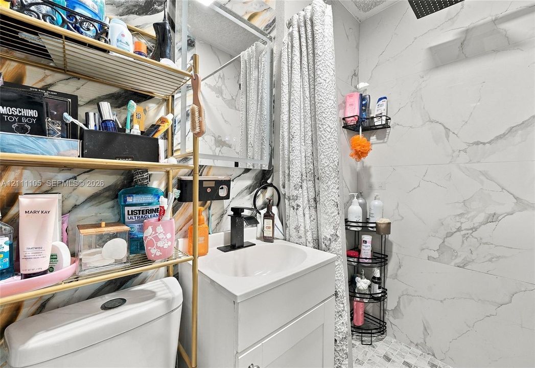 Bathroom featuring large-format veined wall tile, a white vanity with a rectangular basin, a matte black single-handle faucet, a medicine cabinet with a mirror, and a built-in shower niche