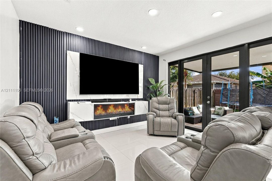 Interior space featuring a dark, vertically-grooved accent wall, a built-in media console with integrated electric fireplace, large-format tile flooring, recessed lighting, and black-framed French doors