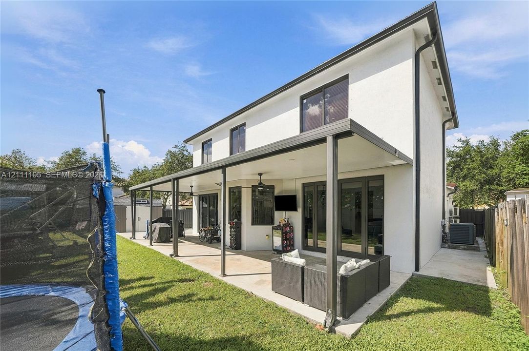 Exterior space featuring a concrete patio, a covered lanai with ceiling fans, dark-trimmed windows, and a fenced yard