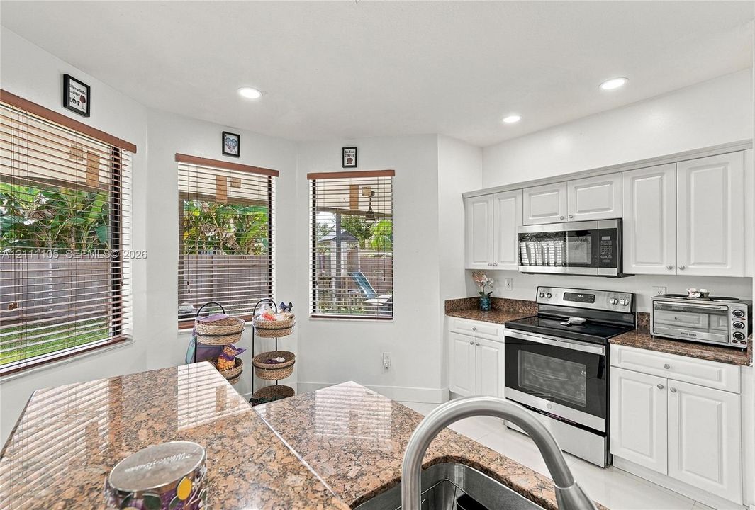 Kitchen featuring white shaker-style cabinetry, stone-finish countertops, recessed lighting, stainless steel appliances, and a trio of windows