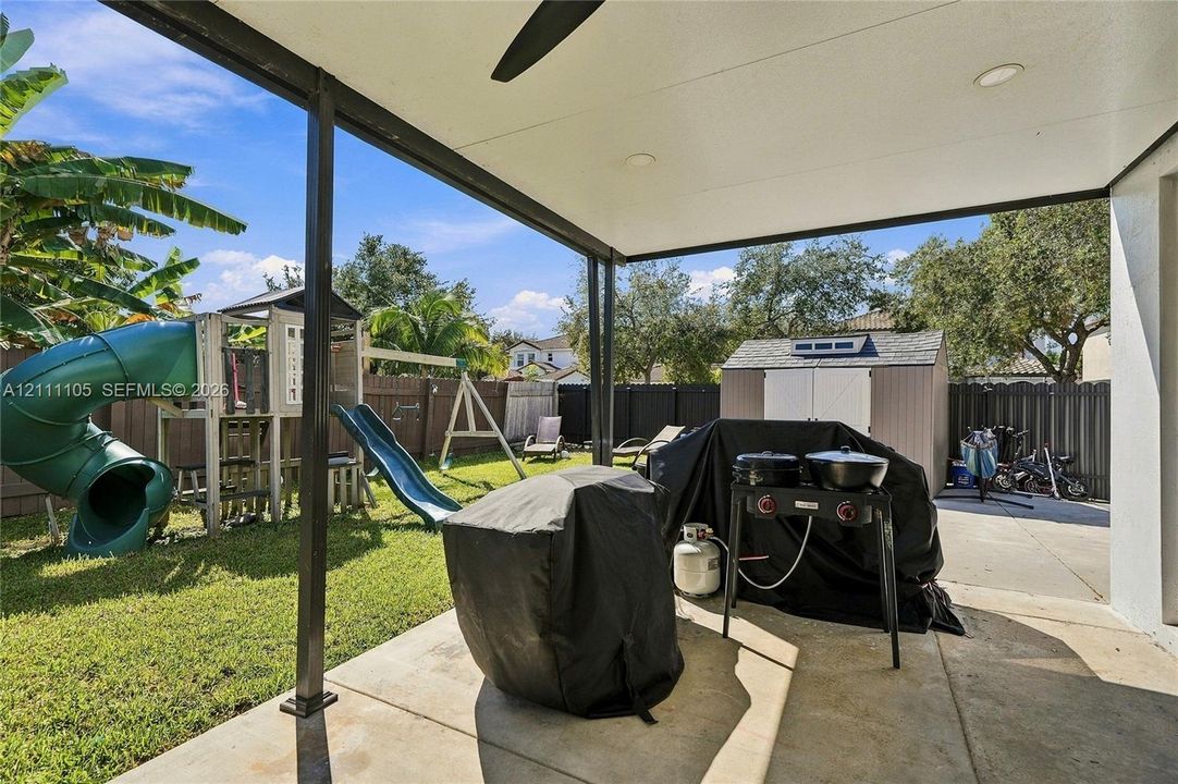 Covered concrete patio featuring a ceiling fan and recessed lighting, overlooking a fenced backyard with a concrete pad and storage shed