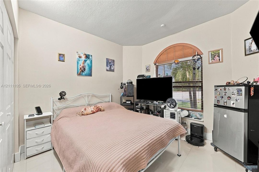 Neutral-toned interior room featuring tile flooring, a multi-paneled closet door, and an arched window with an integrated blind