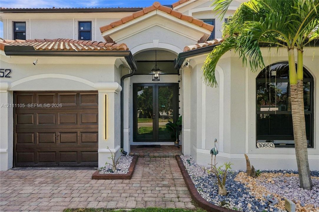 Stucco exterior featuring a terracotta tile roof, arched entryway, brick-paver driveway, and an arched window with decorative molding