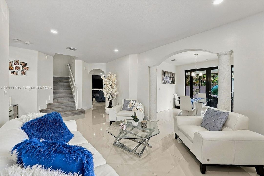 Open floor plan featuring polished tile flooring, arched entryways, structural columns, recessed lighting, and a staircase with wood-finish treads