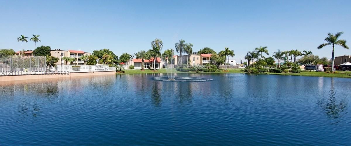 Waterfront grounds featuring a central fountain, manicured lawn, perimeter landscaping, and mature palm trees