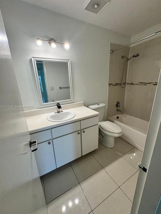 Bathroom featuring a vanity with integrated sink and countertop, framed mirror, three-light fixture, tiled flooring, and a tub with a tile surround