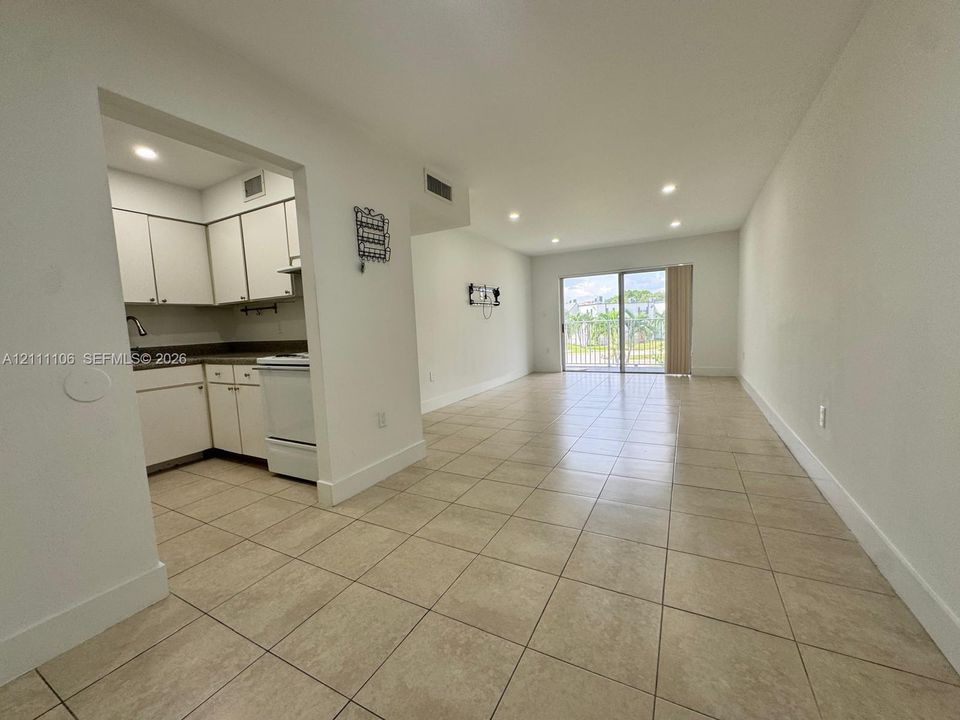 Open-concept interior featuring light-toned tile flooring, recessed ceiling lighting, a kitchen with white cabinetry, and sliding glass doors