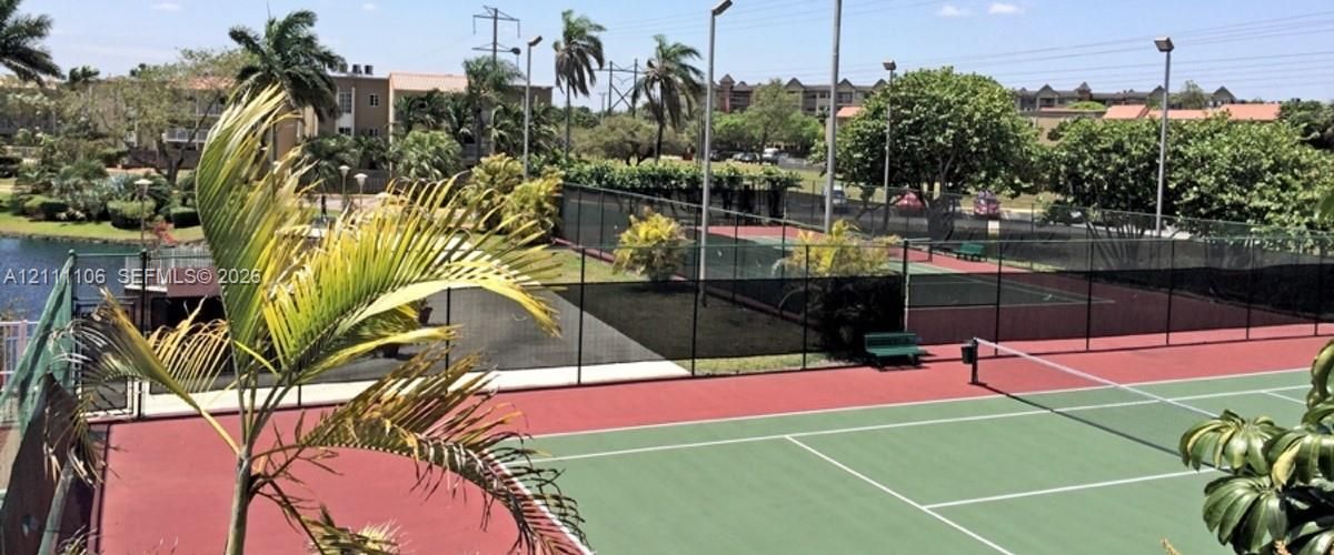 Hard-surface tennis courts with perimeter fencing, stadium-style lighting, and mature landscaping