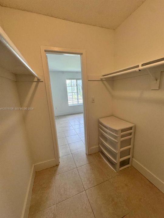 Walk-in closet featuring ceramic tile flooring, dual-level wall-mounted shelving, and hanging rods