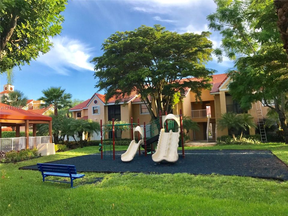 Outdoor recreation area featuring a multi-feature playground structure, rubberized safety surfacing, and a covered pavilion