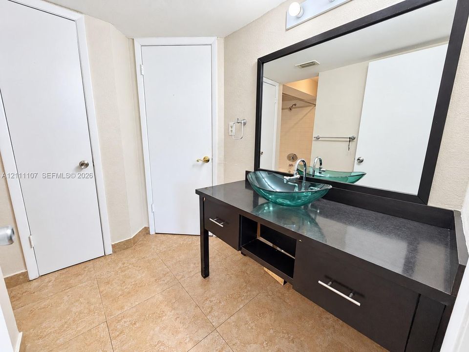 Dark wood-finish vanity with a stone countertop, glass vessel sink, large wall-mounted mirror, and tile flooring