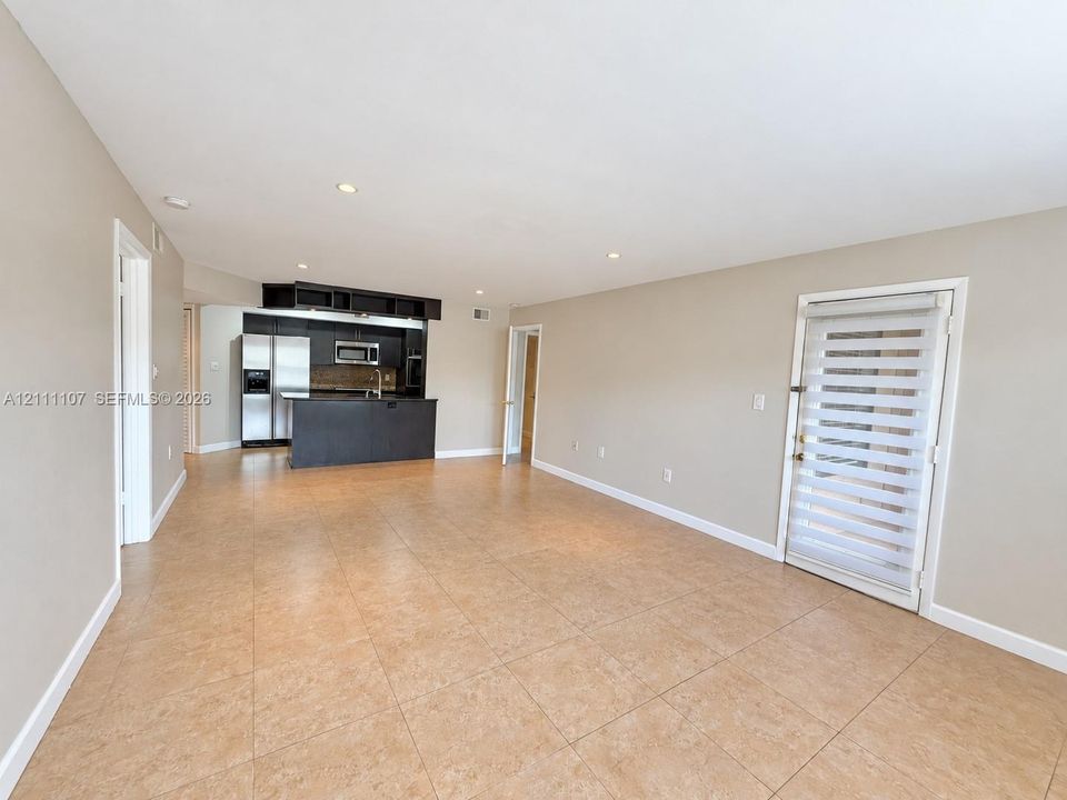 Open-concept interior featuring large-format tile flooring, recessed lighting, and kitchen cabinetry with a central peninsula