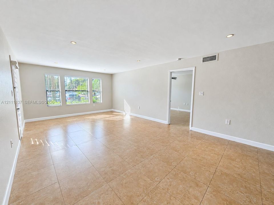 Spacious room featuring neutral wall tones, large-format tile flooring, recessed ceiling lighting, and multiple windows