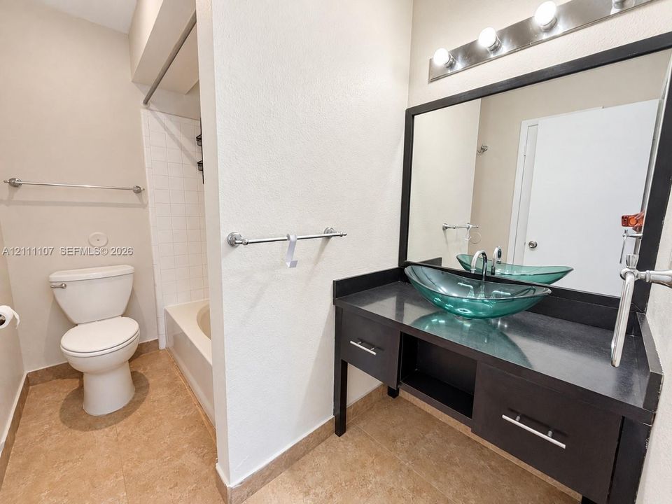 Dark-finish vanity featuring a glass vessel sink, solid-surface countertop, rectangular mirror with a matching frame, and multi-bulb light fixture