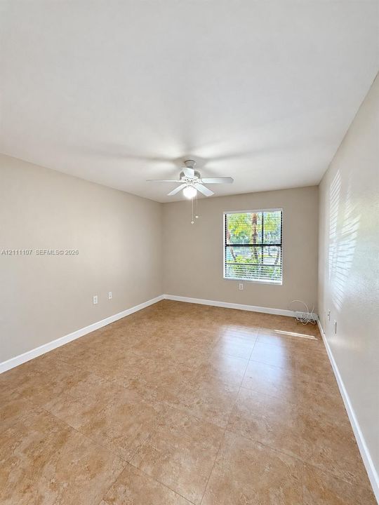 Neutral-toned room featuring large-format tile flooring, a central ceiling fan with integrated light fixture, and a single-pane window