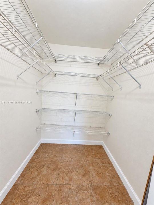 Walk-in storage space featuring multi-level white wire shelving and square tile flooring