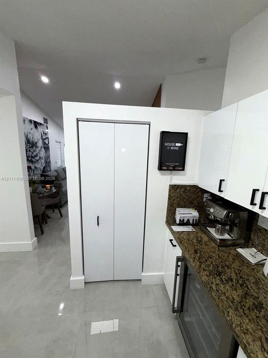 High-gloss white cabinetry, stone countertop, built-in wine refrigerator, and bi-fold closet door with matte black hardware