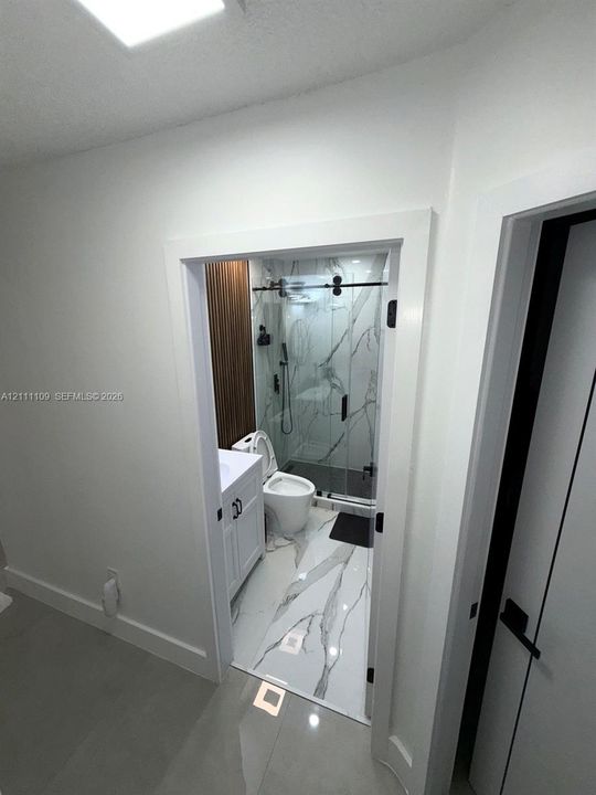 Bathroom featuring large-format tile flooring with marble-style veining, walk-in shower with a sliding glass door, wall-mounted shower hardware, vertical wood-finish wall paneling, and a white vanity cabinet