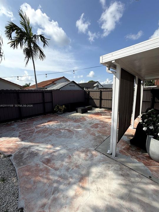 Backyard patio featuring stamped concrete flooring, a covered overhead structure, and full-perimeter privacy fencing