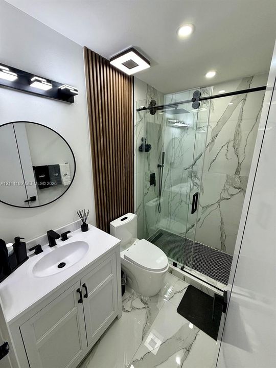 Bathroom featuring a white vanity with a rectangular sink, wall-mounted circular mirror, vertical wood-slat accent wall, shower with glass enclosure, and large-format tile flooring