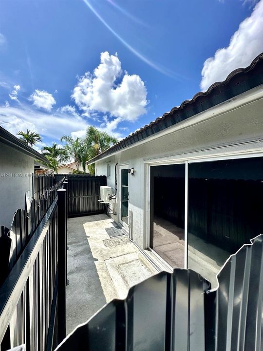 Exterior side yard with concrete hardscaping, sliding glass doors, and a full-perimeter metal privacy fence