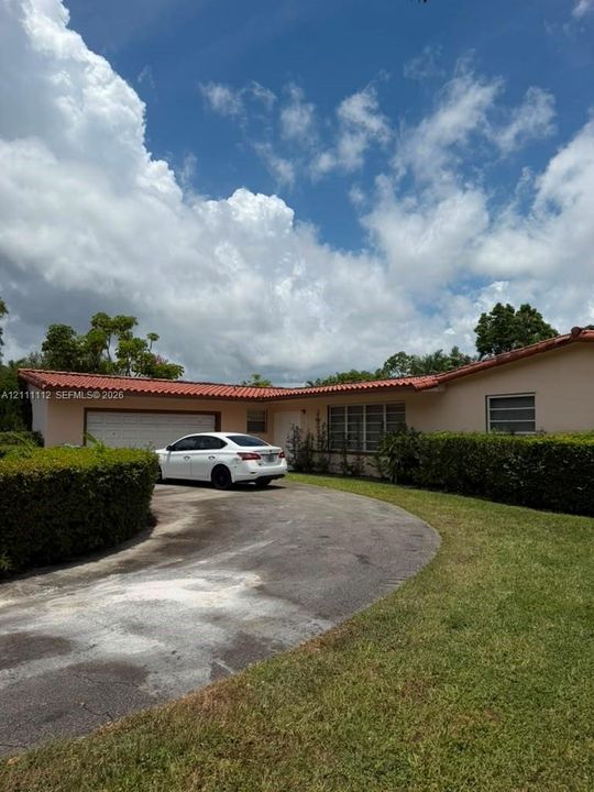Single-story residence featuring a tile roof, paved circular driveway, and manicured landscaping