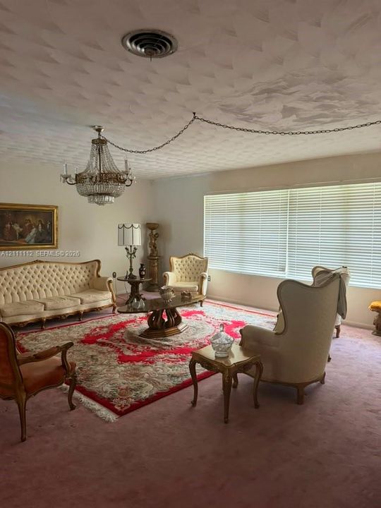 Spacious room featuring a tiered crystal chandelier, wall-to-wall carpeting, and large windows with horizontal blinds