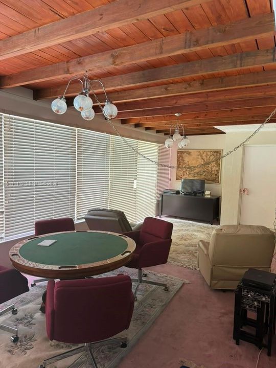 Exposed wood-beam ceiling featuring natural wood-finish planking, two multi-arm globe light fixtures, and floor-to-ceiling windows with horizontal blinds