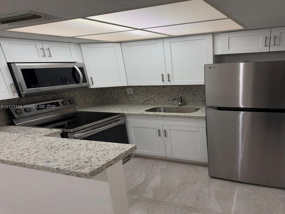 Kitchen featuring white Shaker-style cabinetry, speckled stone-look countertops, stainless steel appliances, a drop-in stainless steel sink, and recessed panel lighting