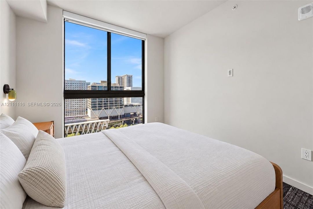 Floor-to-ceiling window featuring city scenery, wall-mounted modern sconce, and textured dark carpeting