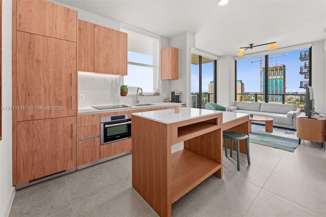 Kitchen featuring wood-finish cabinetry, stone-surface countertops, an integrated island with built-in storage, large-format tile flooring, and floor-to-ceiling windows