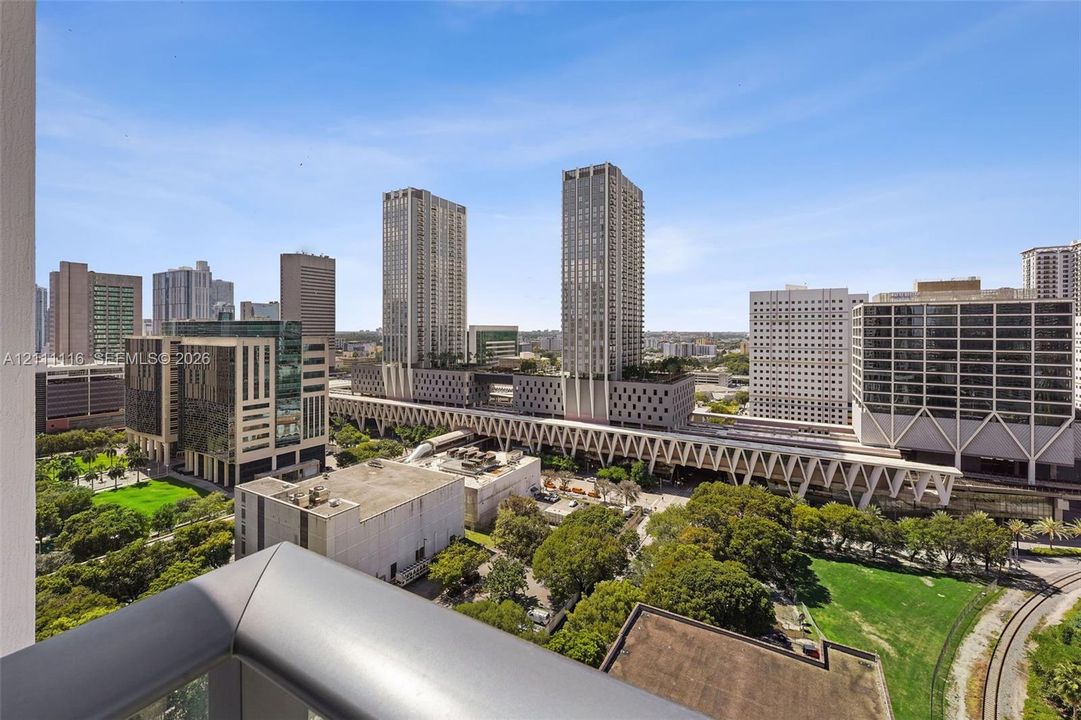 Outdoor balcony with metal railings overlooking an urban cityscape featuring high-rise buildings, green spaces, and infrastructure