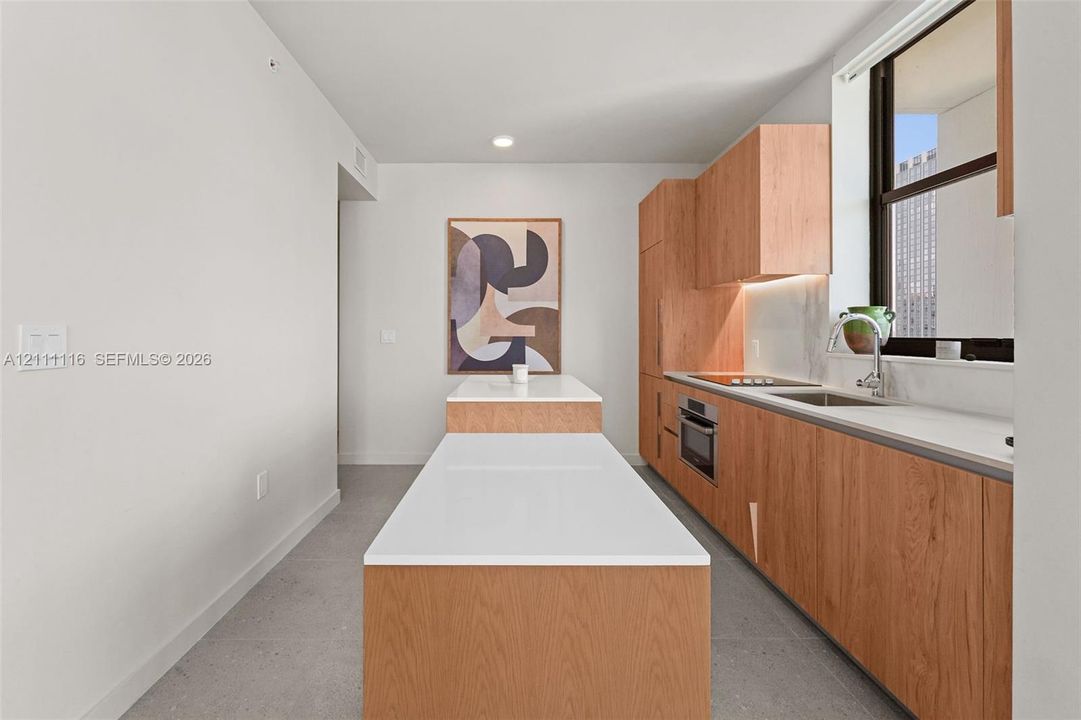 Kitchen featuring wood-finish cabinetry, stone-surface countertops, an integrated island, stainless steel sink with a pull-down faucet, and a built-in cooktop