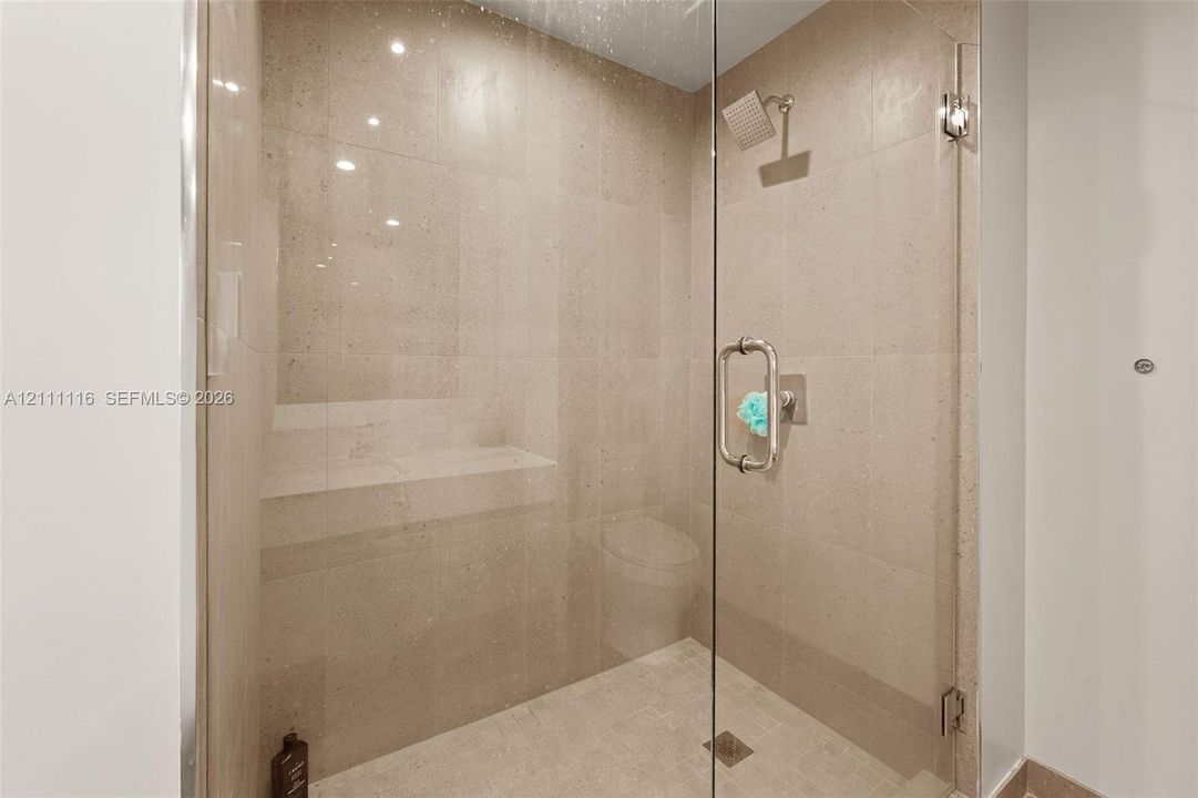 Walk-in shower featuring large-format tile surround, glass enclosure, built-in recessed shelving, rainfall shower head, and polished metal hardware